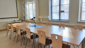 Kokoushuoneessa on yhdistettäviä pöytiä, jotka ovat muodostaneet ison pöydän. Kummallakin puolella pöytää on kuusi puutuolia.