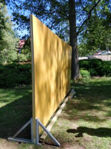 Puistomaisemassa keltasävyisellä pohjamaalilla oleva graffitiseinä sivustapäin kuvattuna.